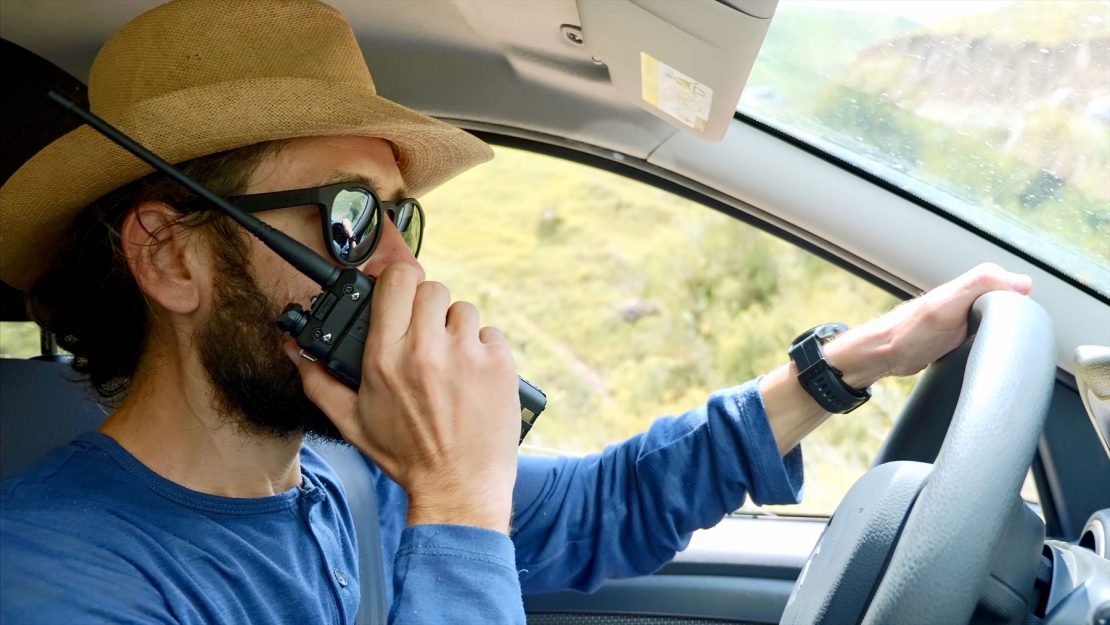 Guy in hat talking on two-way radio while driving.
